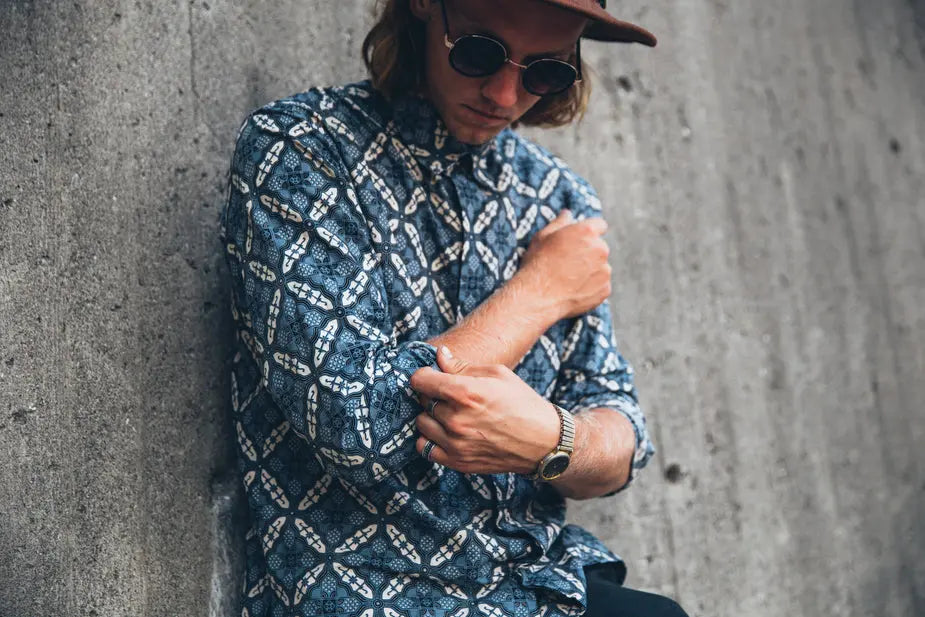 Handmade ocean blue shirt with geometric pattern worn by man against concrete wall.