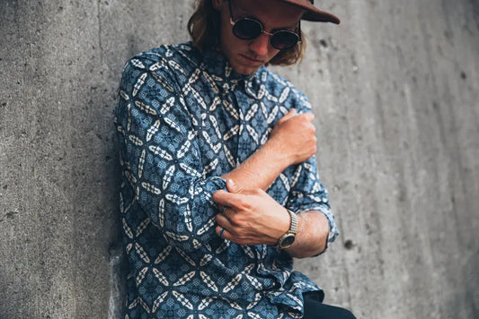 Handmade ocean blue shirt with geometric pattern worn by man against concrete wall.